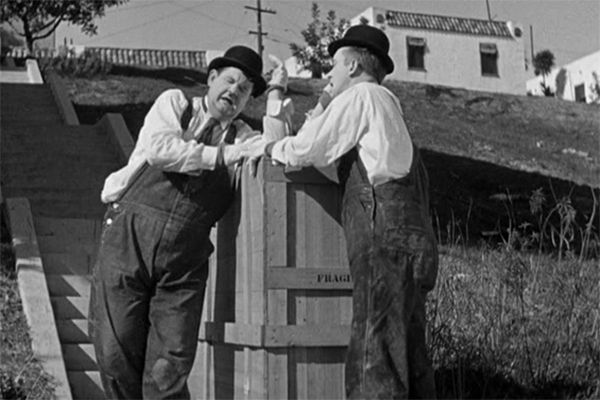 two men standing next to each other in front of a wooden structure with grass on the ground