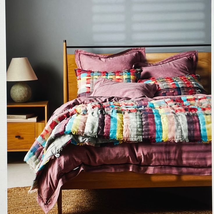 a bed with colorful blankets and pillows in a room next to a night stand on the floor