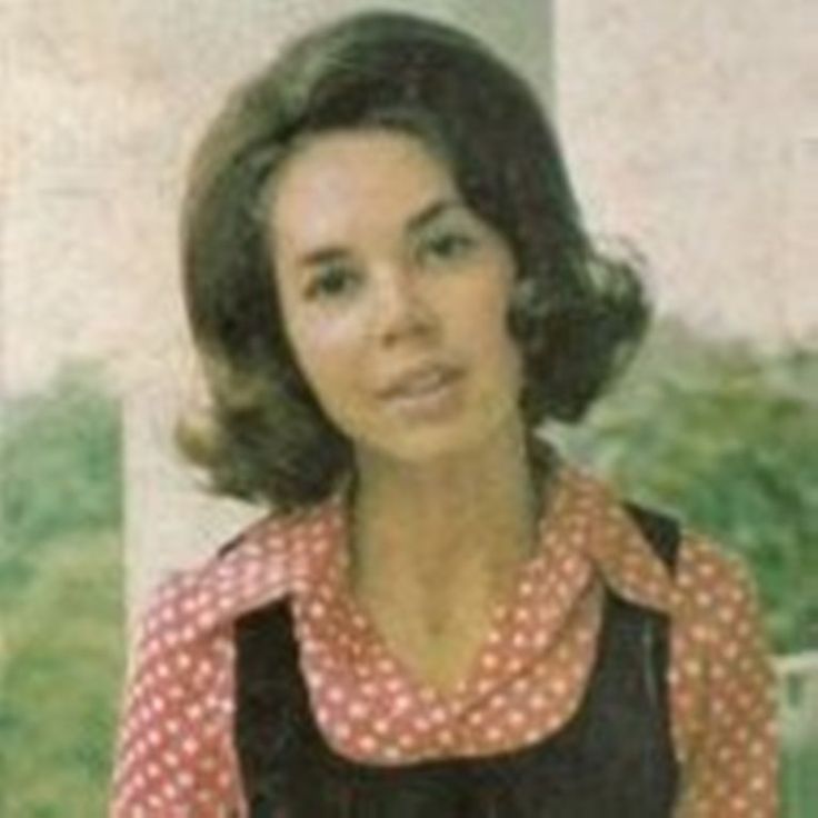 an old photo of a woman wearing a polka dot shirt and black overalls, standing in front of a building