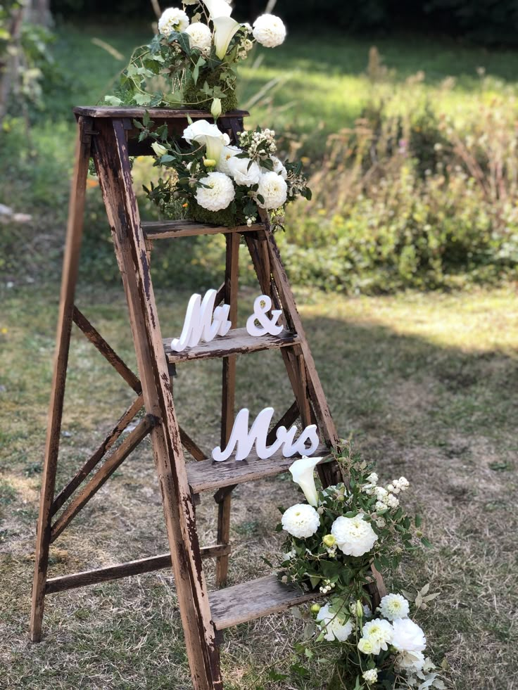 an old ladder decorated with flowers and mr and mrs signs for the wedding ceremony is shown