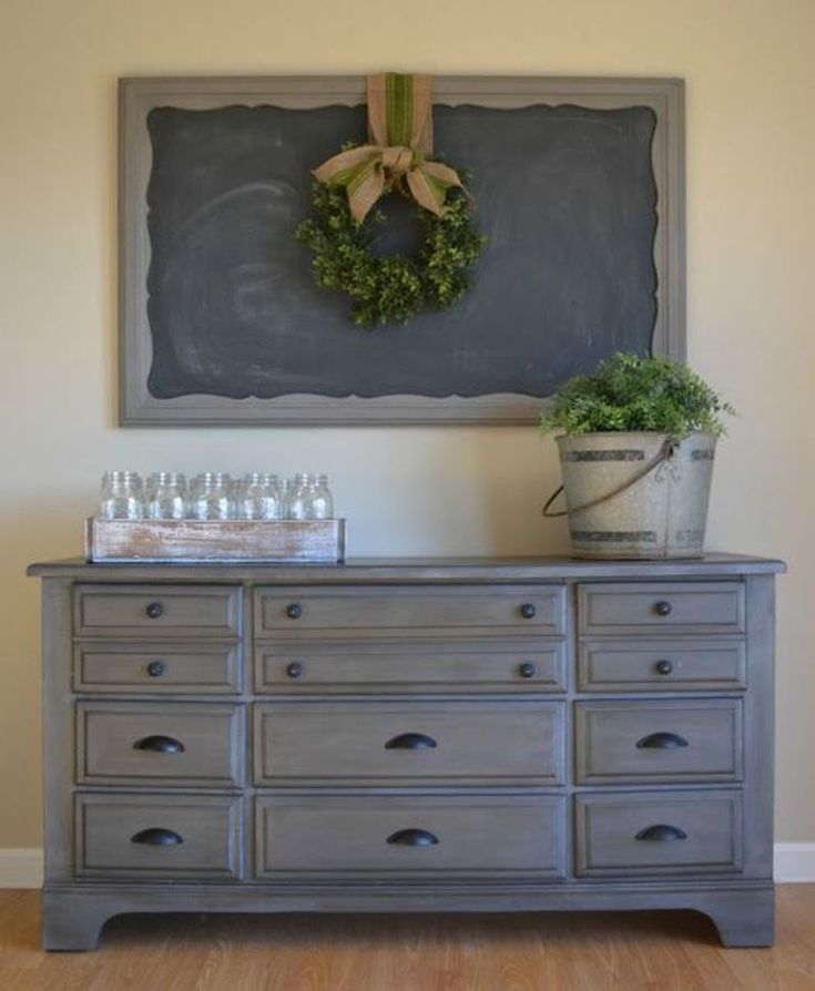 a gray dresser with a chalkboard and wreath on the wall above it, filled with glasses