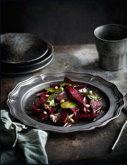 a plate with beets and pistachios on it next to a cup