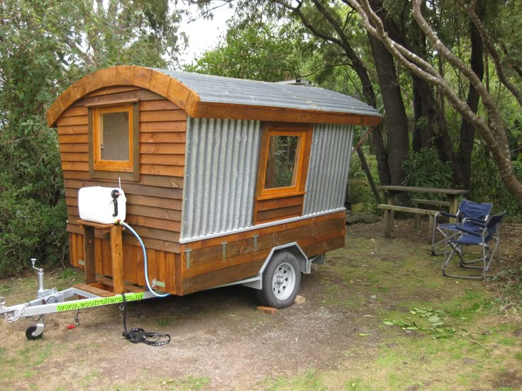 a tiny house on wheels is parked in the grass next to some chairs and trees