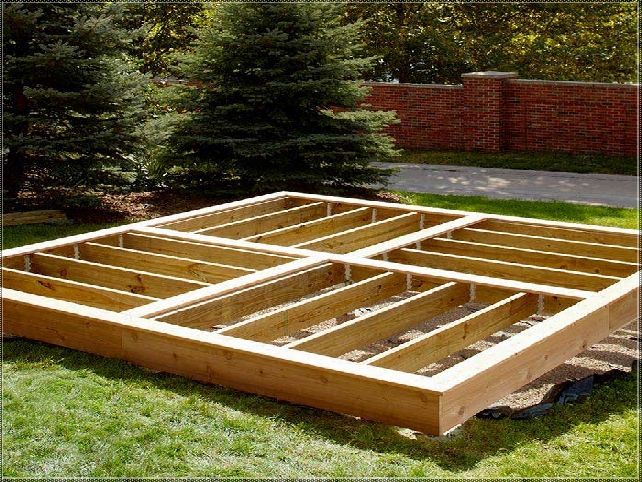 a wooden bed frame sitting in the middle of a grass covered yard next to trees