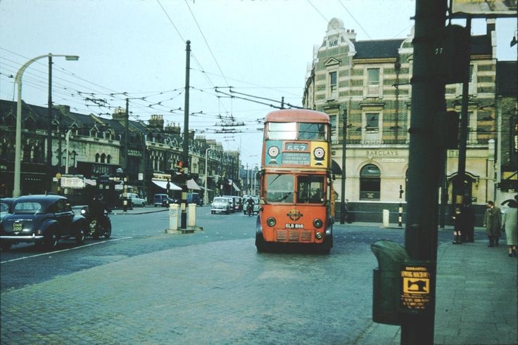 a red double decker bus driving down a street next to tall buildings and power lines