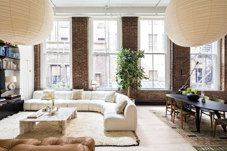 a living room filled with lots of furniture next to tall windows in a brick building