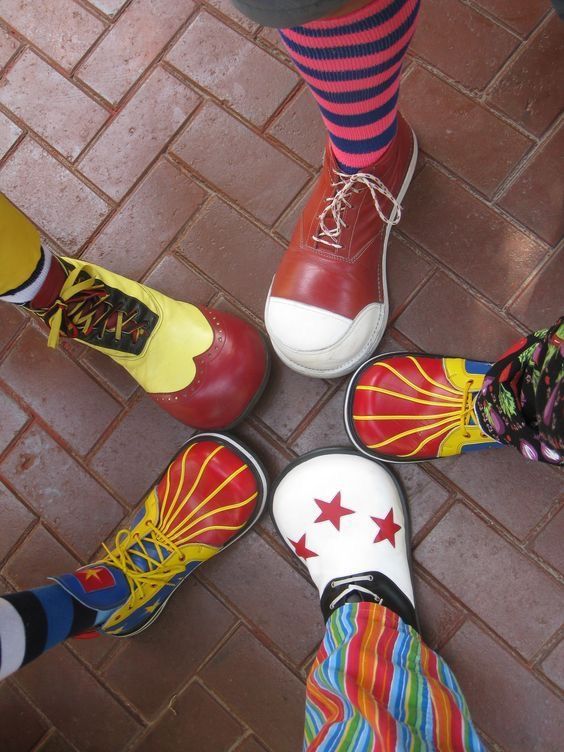 four pairs of brightly colored shoes stand in a circle on a brick floor with colorful socks