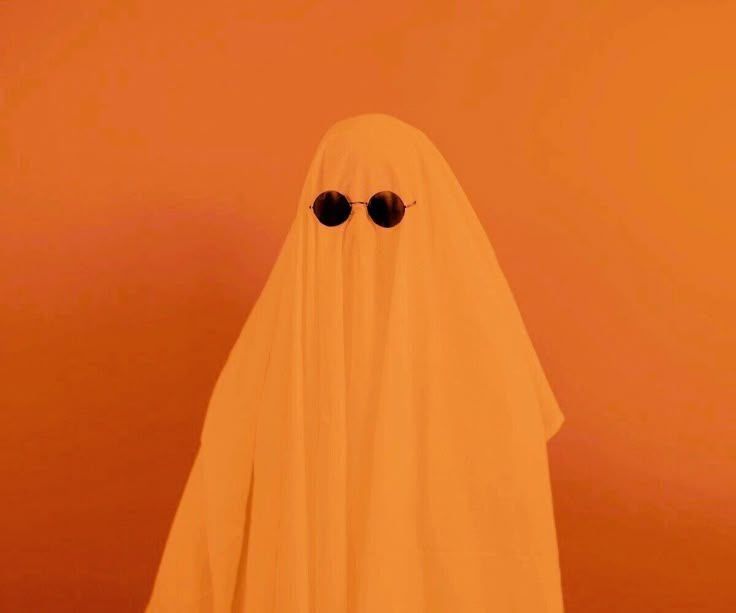 a white ghost with sunglasses on it's face and eyes are standing in front of an orange wall