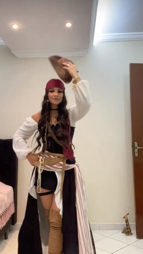 a woman dressed in pirate garb and holding a hat on her head while standing next to a bed