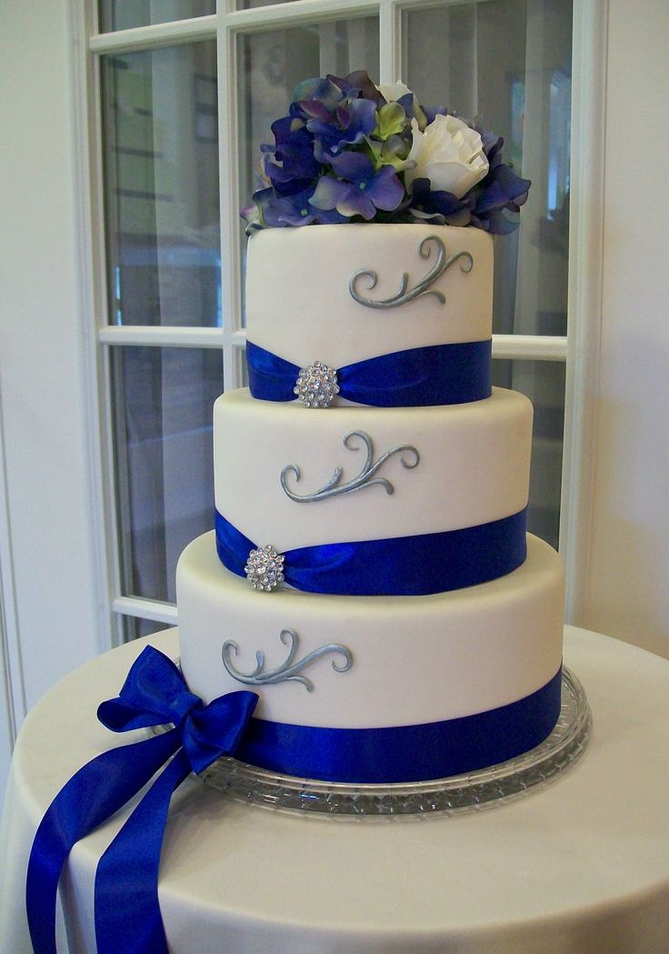 a three tiered wedding cake with blue ribbon and flowers