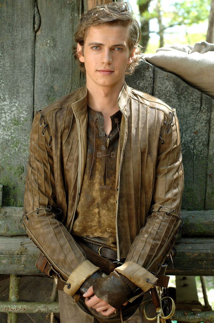 a young man dressed in medieval clothing and holding an elephant's trunk while standing next to a wooden fence