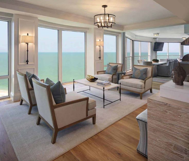 a living room filled with lots of furniture and large windows overlooking the ocean in front of them