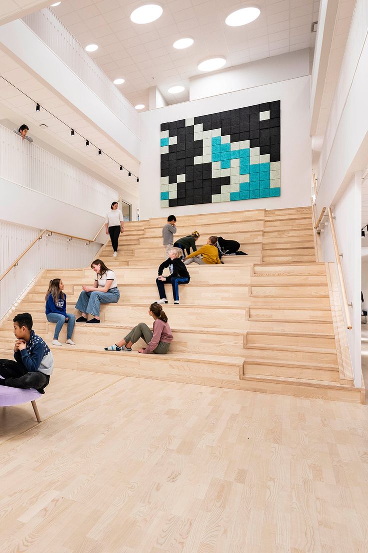 several people are sitting on the stairs in an empty building with white walls and wood flooring