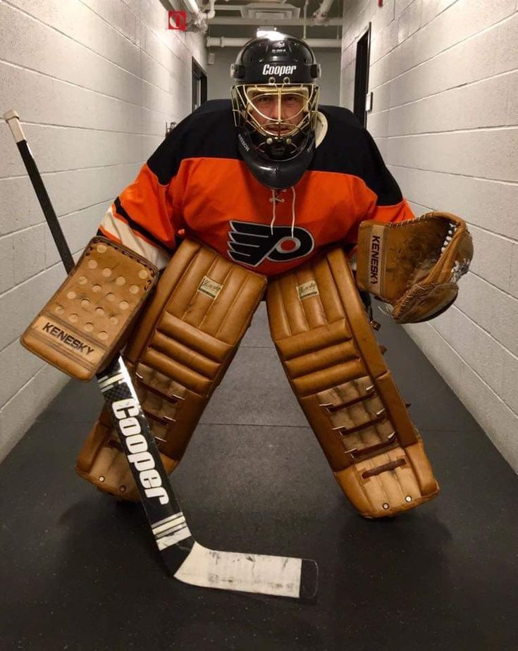 a hockey goalie in an orange and black jersey with his hands on his knees