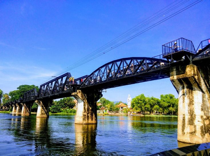 people are walking across a bridge over the water on a sunny day with blue skies