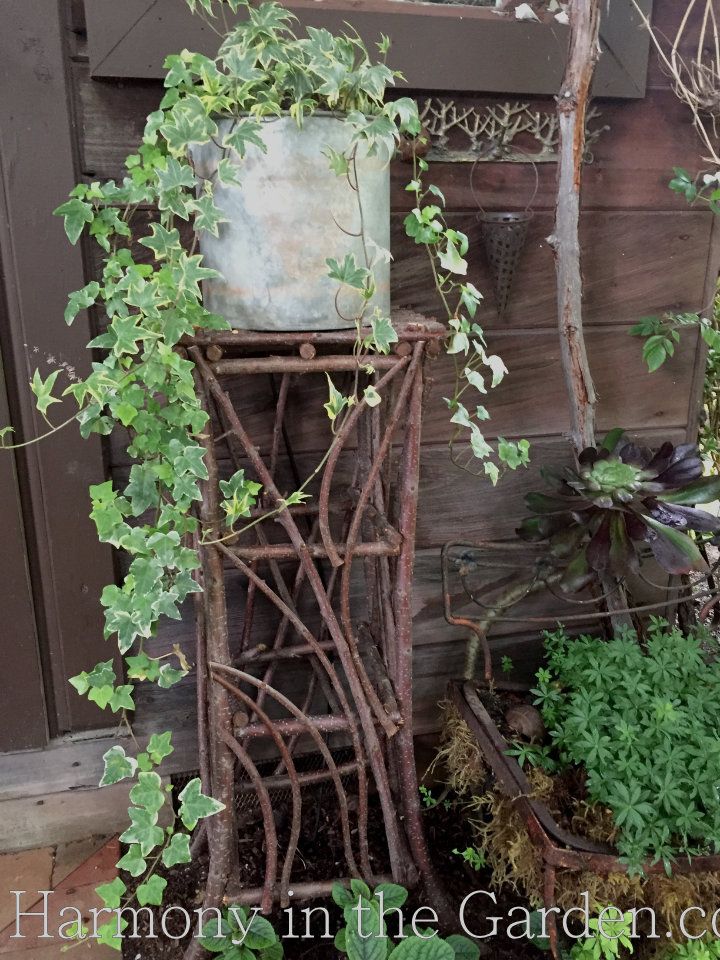 an old metal plant stand sitting next to a wooden fence with ivy growing on it