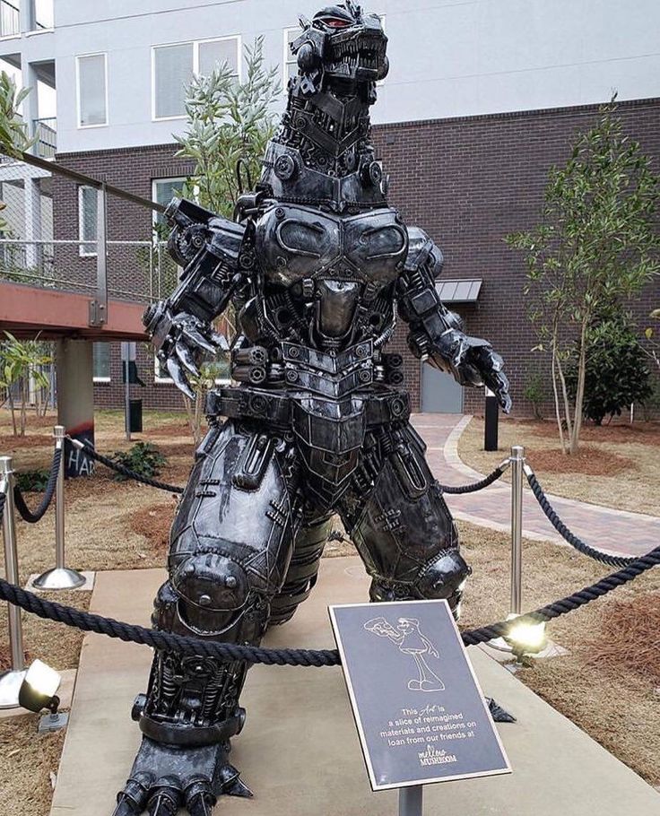 a statue of a robot standing next to a roped off area in front of a building