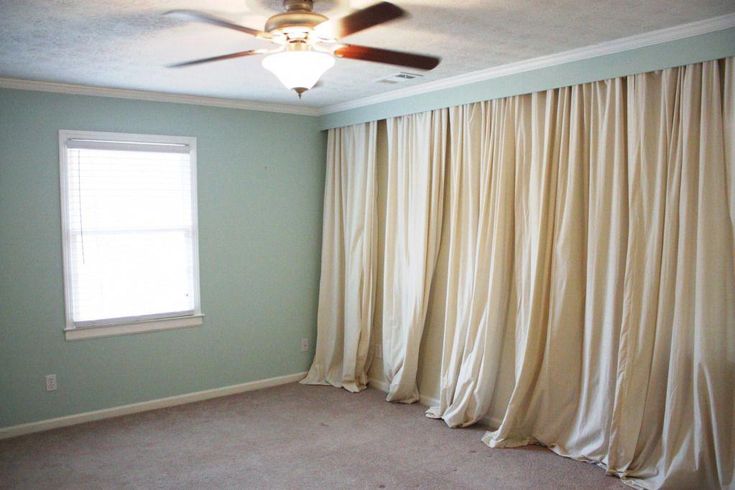 an empty room with a ceiling fan and curtains