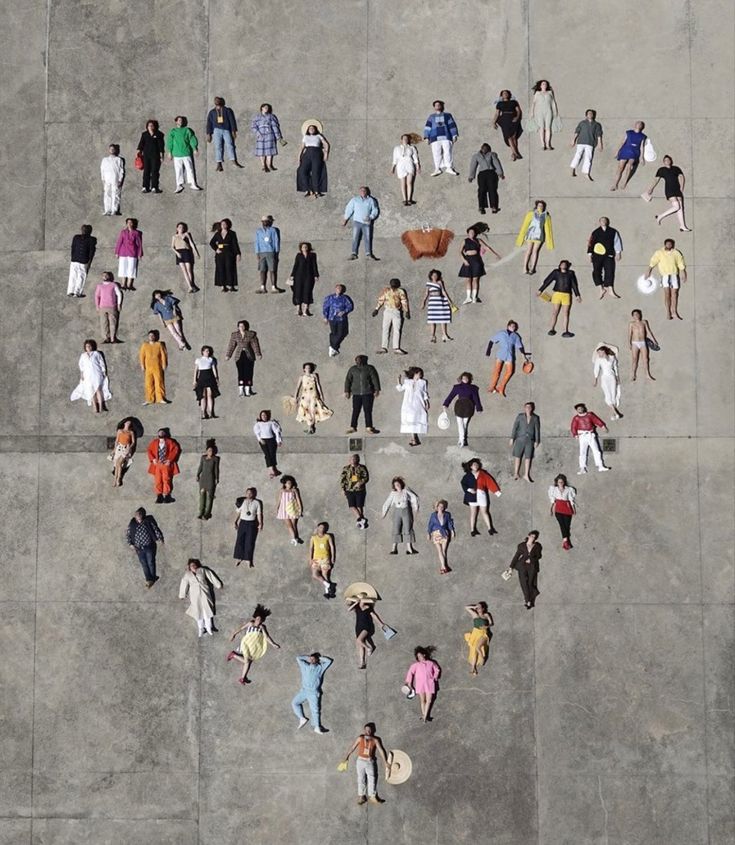 a group of people standing in the shape of a heart on top of a cement floor