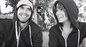 two people sitting next to each other wearing hoodies and sweatshirts smiling at the camera