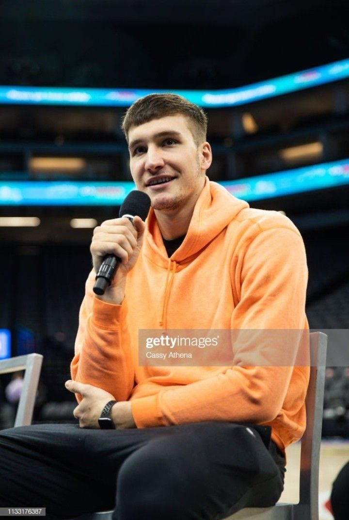 a man in an orange hoodie is sitting on a chair and holding a microphone