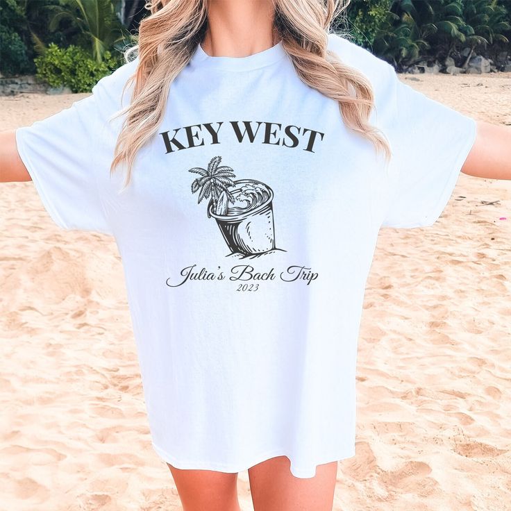 a woman on the beach wearing a key west t - shirt and sunglasses with her arms outstretched