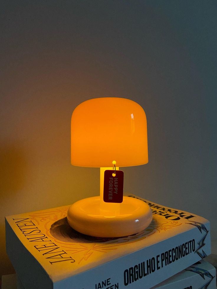 a yellow lamp sitting on top of a white box next to a book and remote control