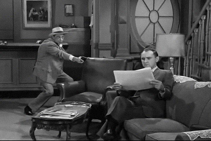 two men in suits and hats are sitting on a couch with papers while another man is standing behind them