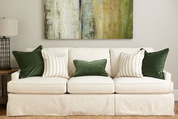 a white couch with green pillows and a painting on the wall