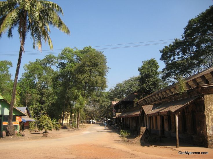 a dirt road with buildings and trees on both sides