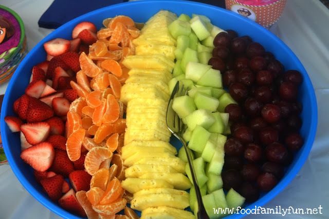 a blue bowl filled with sliced fruit next to yogurt and strawberries on a table