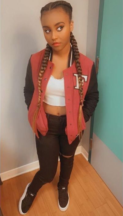 a woman with braids standing in front of a door wearing a red jacket and black pants