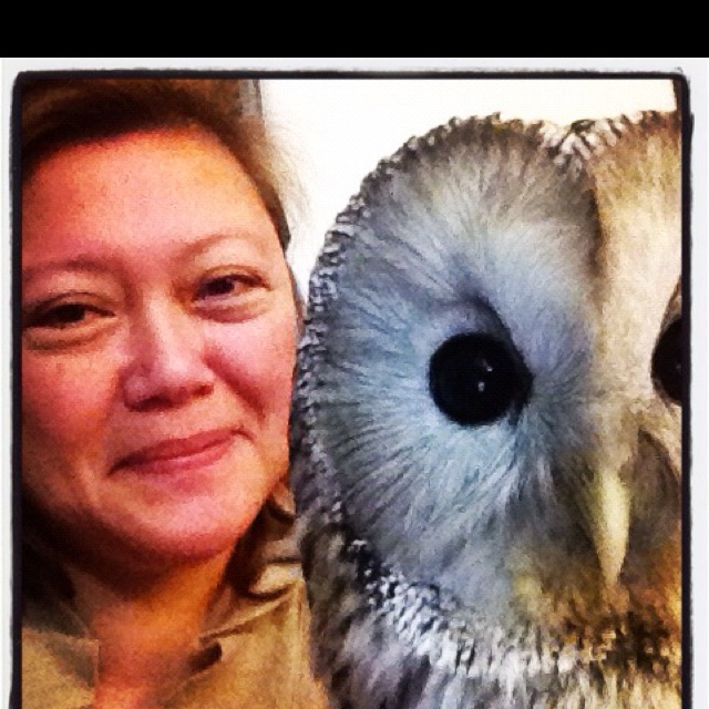 a woman is holding an owl's head in front of her