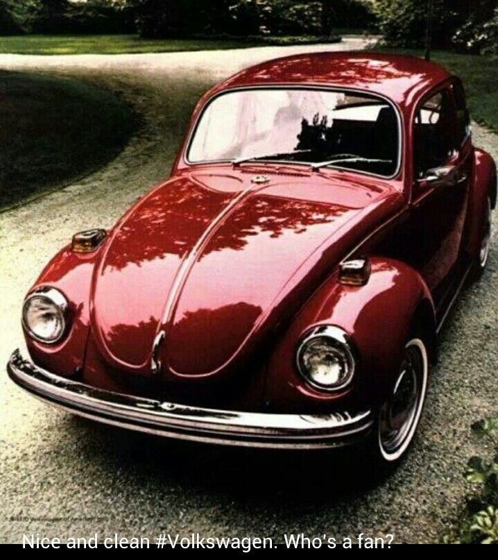 an old red vw bug parked on the side of a road in front of some trees