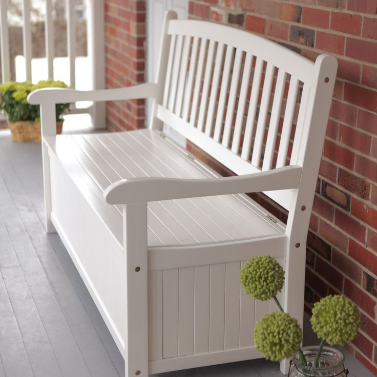 a white bench sitting next to a brick wall with potted plants on the side