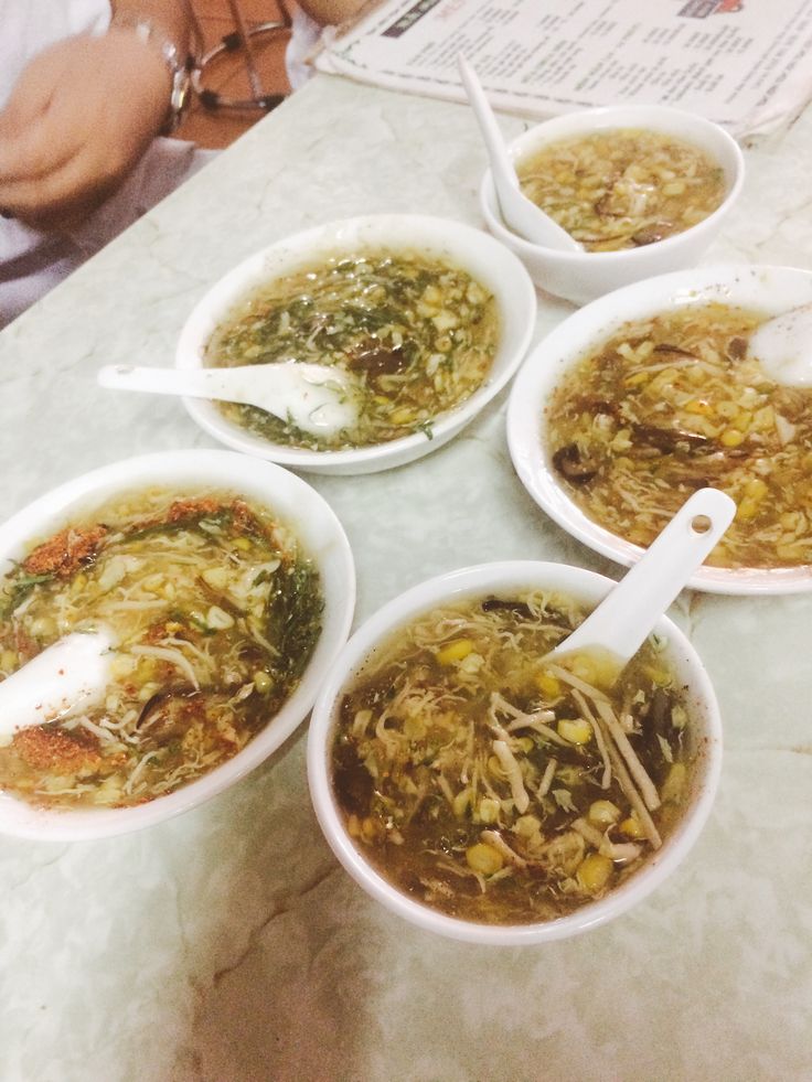 four bowls of food are on the table with spoons in them and one bowl is filled with soup