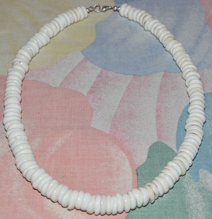 a white beaded necklace on a pink and blue floral print tablecloth with a silver clasp