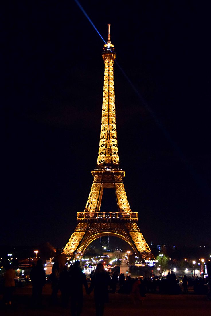 the eiffel tower lit up at night with people standing around in front of it