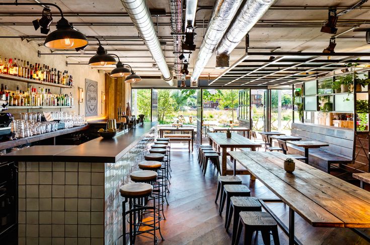 the inside of a restaurant with wooden tables and bar stools, hanging lights, and lots of bottles