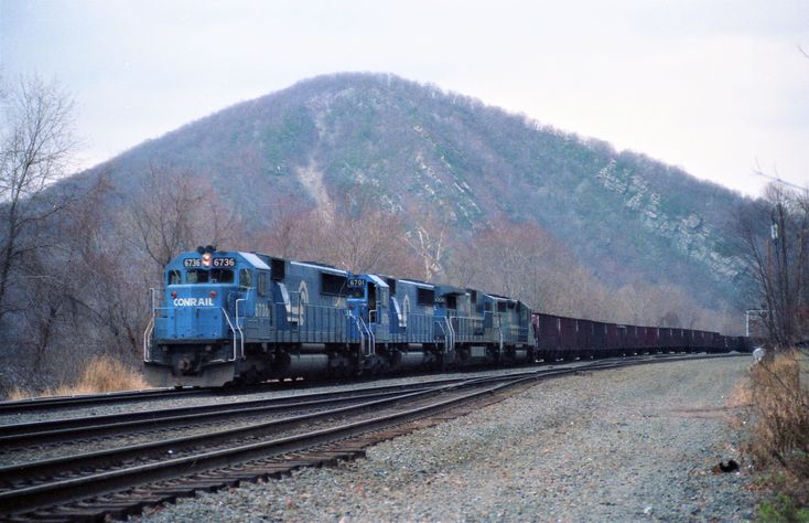 a blue train traveling down tracks next to a mountain