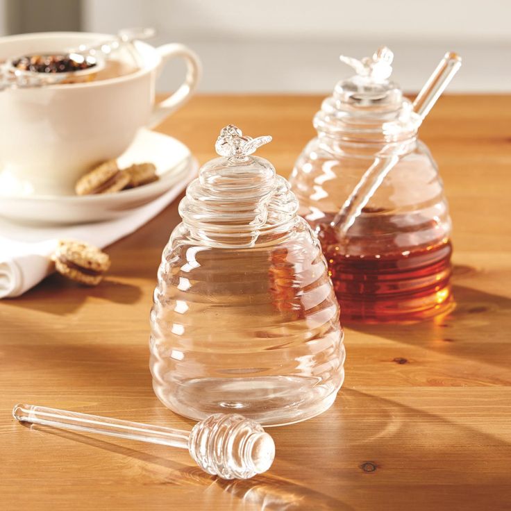 two honey jars sitting on top of a wooden table next to crackers and spoons