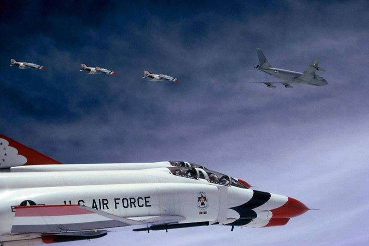 an air force jet flying in the sky with four jets behind it and another plane above