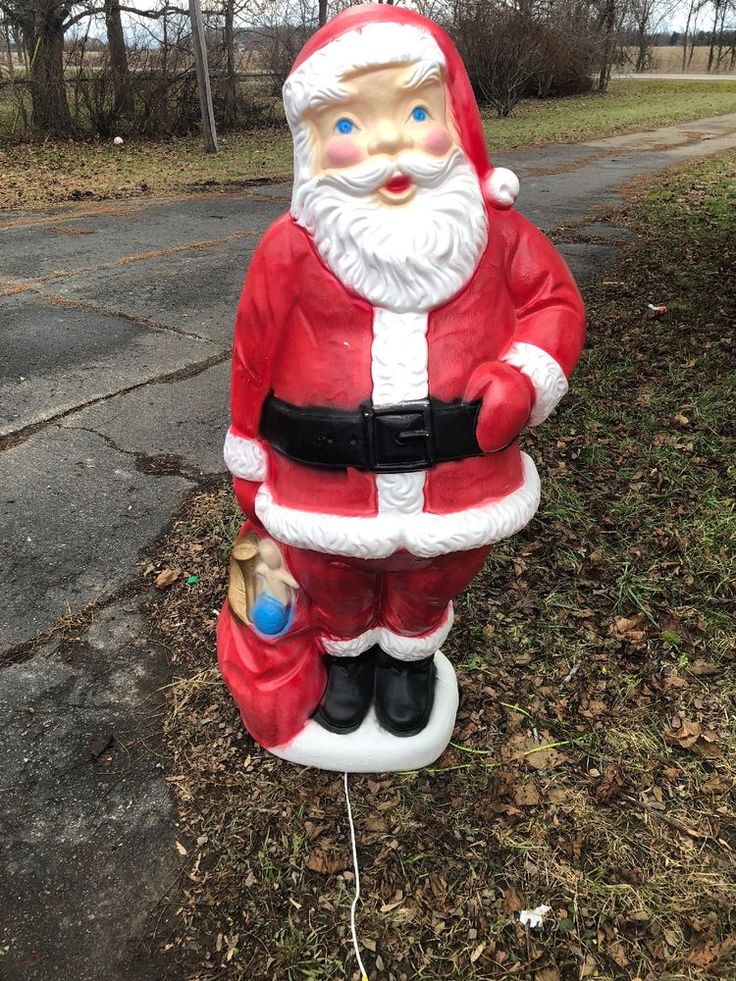 a statue of santa claus is on the side of the road in front of some trees