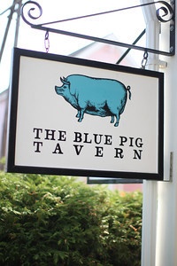 the blue pig tavern sign is hanging from a pole