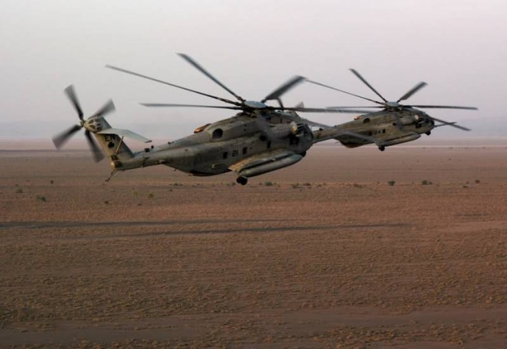 an army helicopter is flying in the sky over desert land and dirt area with no one around it