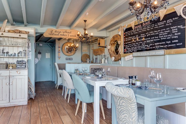 the inside of a restaurant with wooden floors and white tables, blue chairs and chalkboard menus on the wall