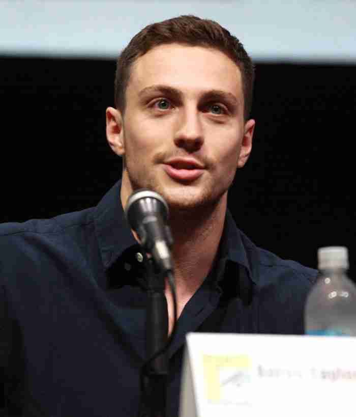 a man sitting at a table with a microphone in front of him and a bottle of water behind him