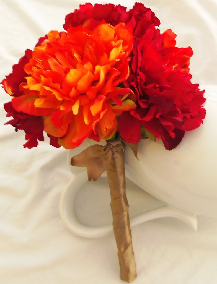 a bouquet of red and orange flowers sitting on top of a white vase