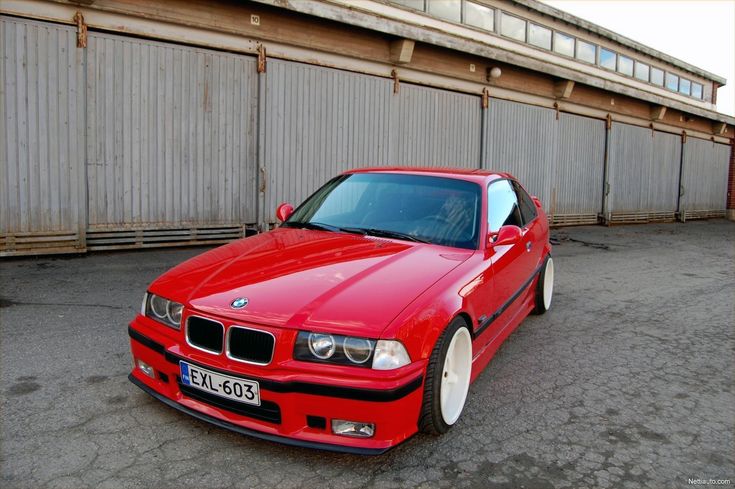 a red car is parked in front of a building with a metal fence behind it