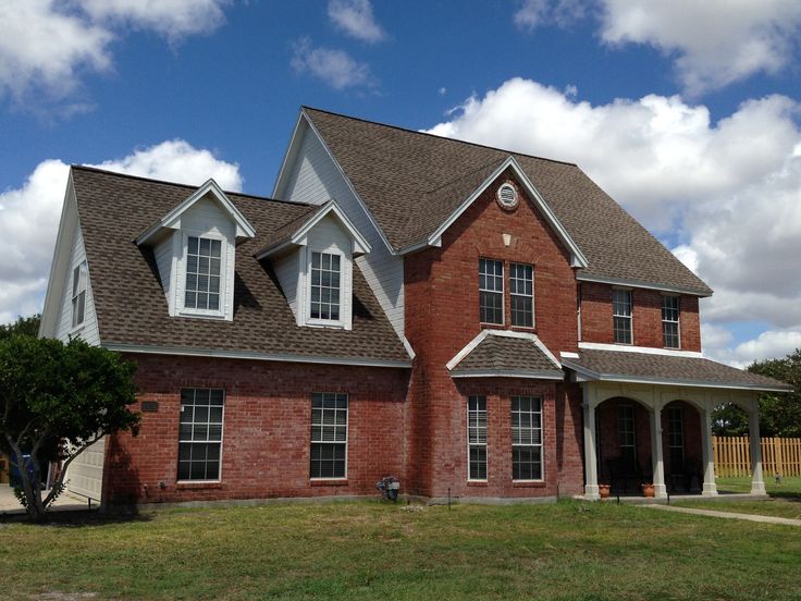 a red brick house with white trim on the roof and two story windows, in front of a blue cloudy sky